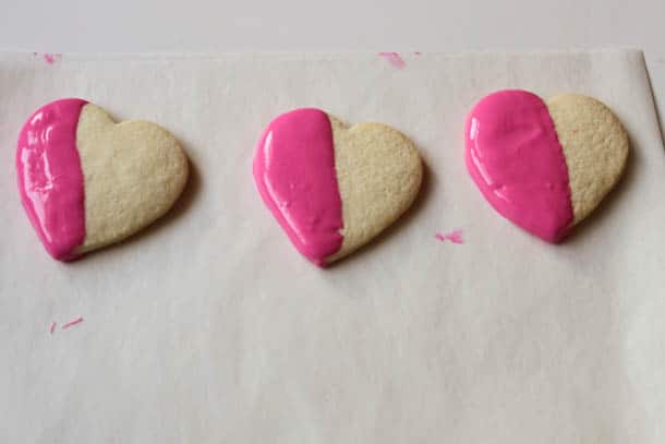 Three gluten-free heart shaped cookies half dipped in pink chocolate.