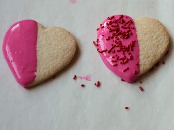 Two gluten-free heart shaped cookies half dipped in pink chocolate.