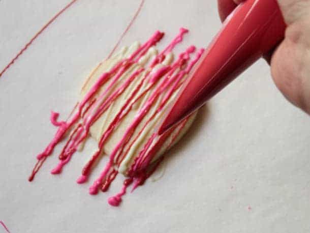 Drizzling a gluten-free cookie with red melted chocolate.