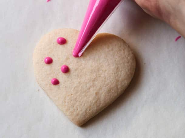 Piping pink chocolate polka dots on gluten-free heart cookie.