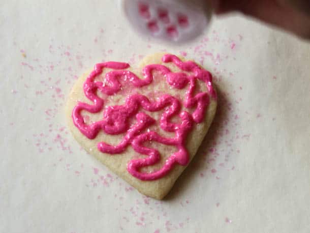 Sprinkling edible glitter on a gluten-free sugar cookie.
