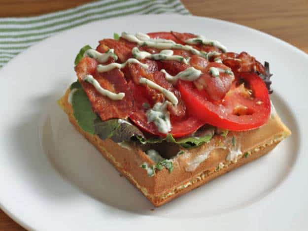 Gluten-Free Waffle BLT on a white plate. BLT is drizzled with basil mayo.