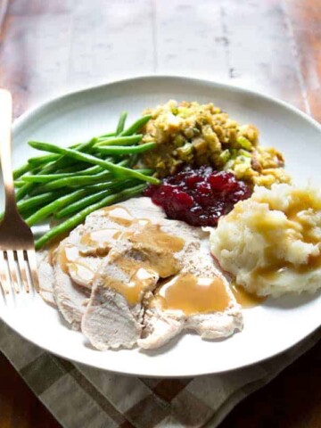 Gluten-free gravy on turkey on a plate of Thanksgiving food.