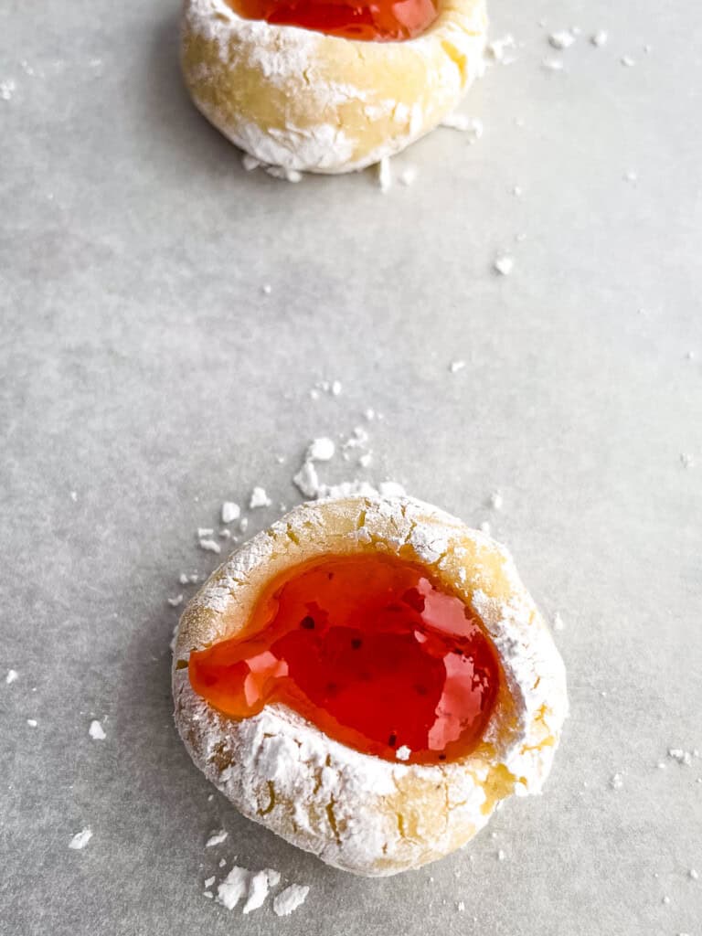 Gluten-free jam thumbprint dough rolled in powdered sugar and topped with jam on a baking sheet.