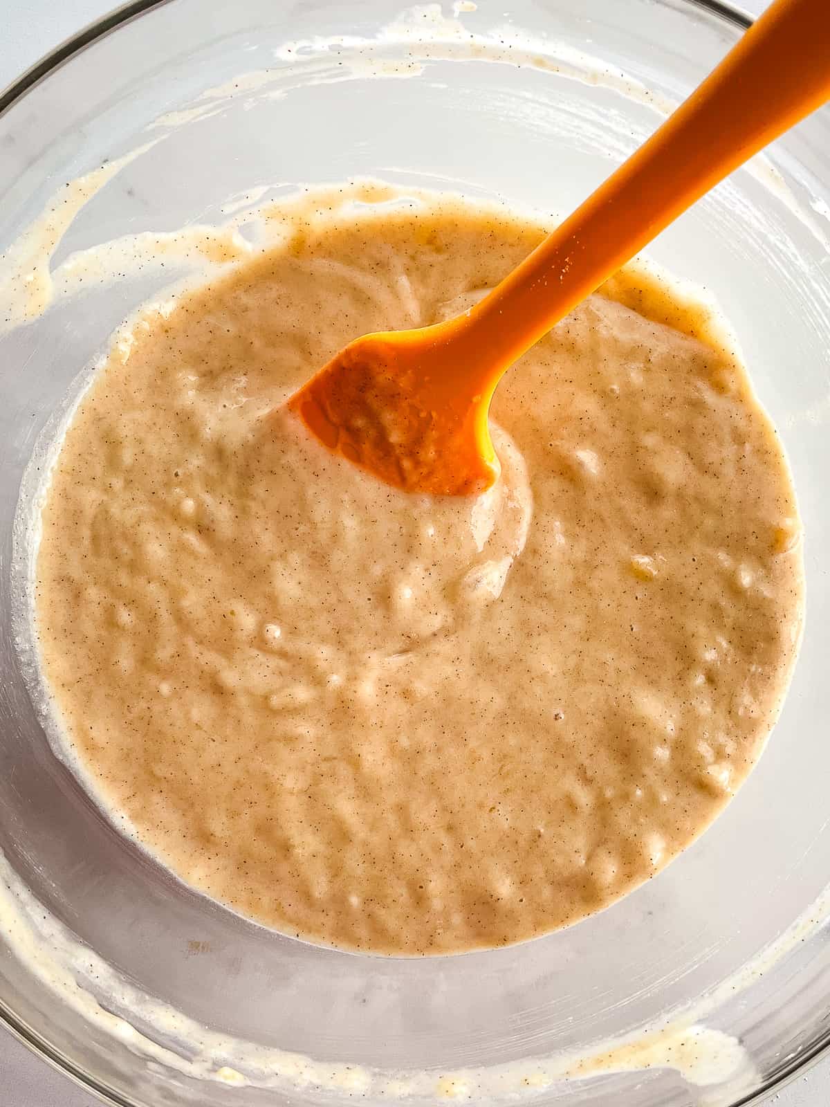 Gluten-free banana pancake batter in a bowl with an orange spatula.