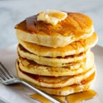 A stack of gluten-free pancakes topped with maple syrup and butter on a plate.