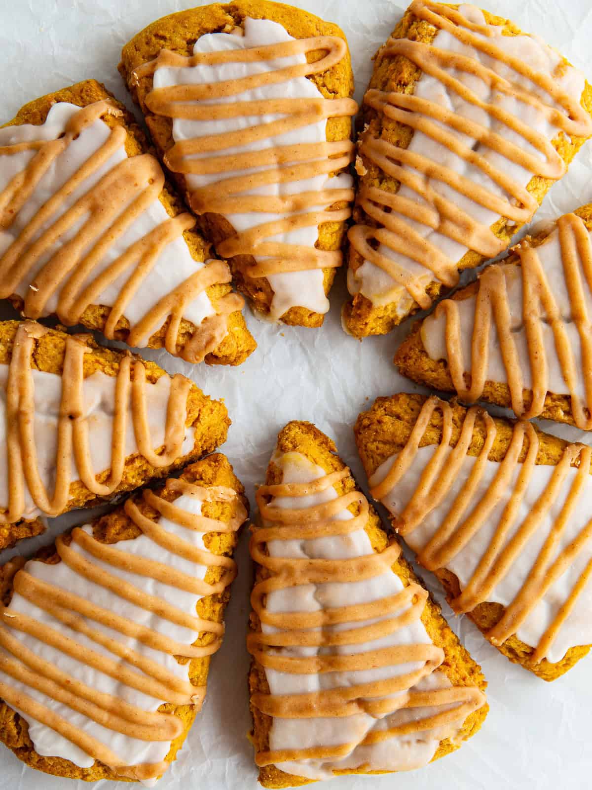 Gluten-free pumpkin scones, finished with vanilla glaze and pumpkin glaze, on parchment paper.