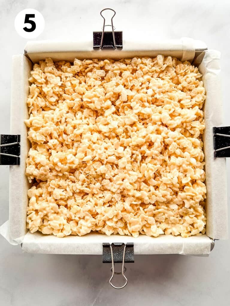 Gluten-free marshmallow crispy treats in a pan. The parchment on the pan is held in place by black binder clips.
